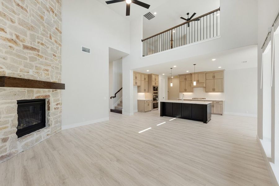 Open-concept living area with stone fireplace, high ceilings, and kitchen with dark island and light wood cabinets visible in background.