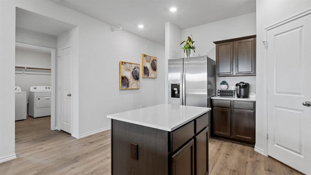 Kitchen featuring dark wood finish cabinets, stainless steel fridge, a center island, light wood-type flooring, and washing machine and clothes dryer Kitchen featuring dark wood finish cabinets, stainless steel fridge, a center island, light wood-type flooring, and washing machine and clothes dryer