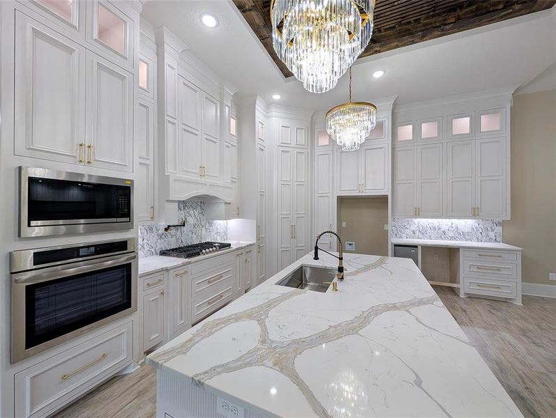 Kitchen featuring tasteful backsplash, light stone countertops, glass insert cabinets, stainless steel appliances, and recessed lighting