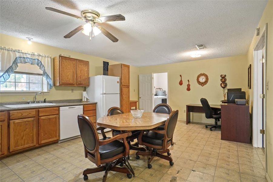 Kitchen with white appliances, brown cabinets, a textured ceiling, a ceiling fan, and a desk