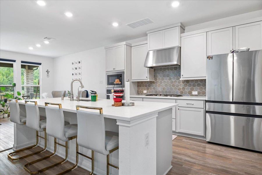 Kitchen with stainless steel appliances, decorative backsplash, under cabinet range hood, an island with sink, and a breakfast bar