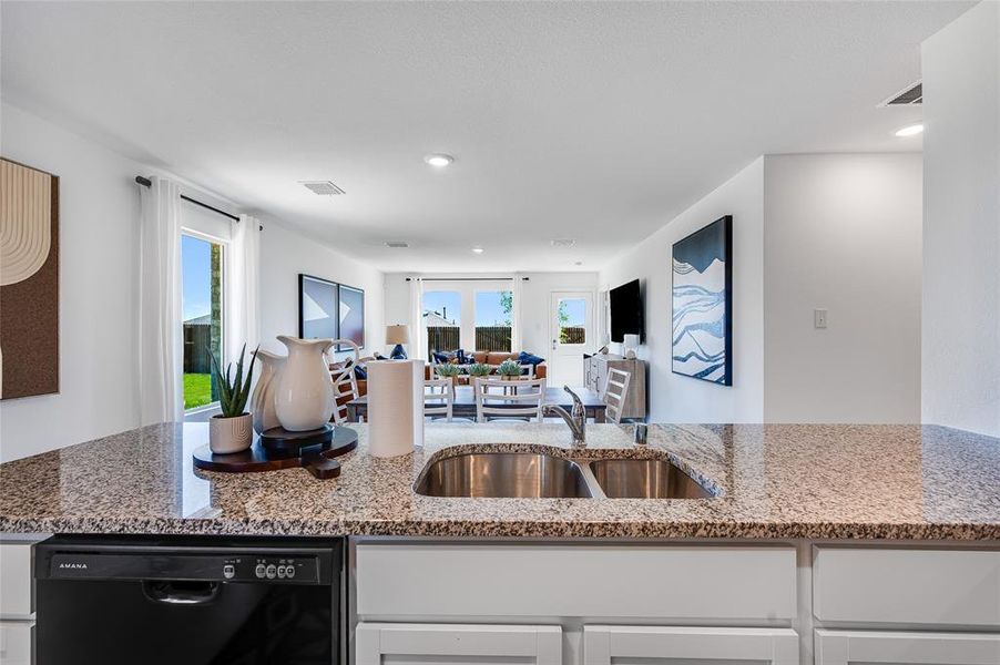 Kitchen featuring plenty of natural light, black dishwasher, white cabinetry, and light stone countertops