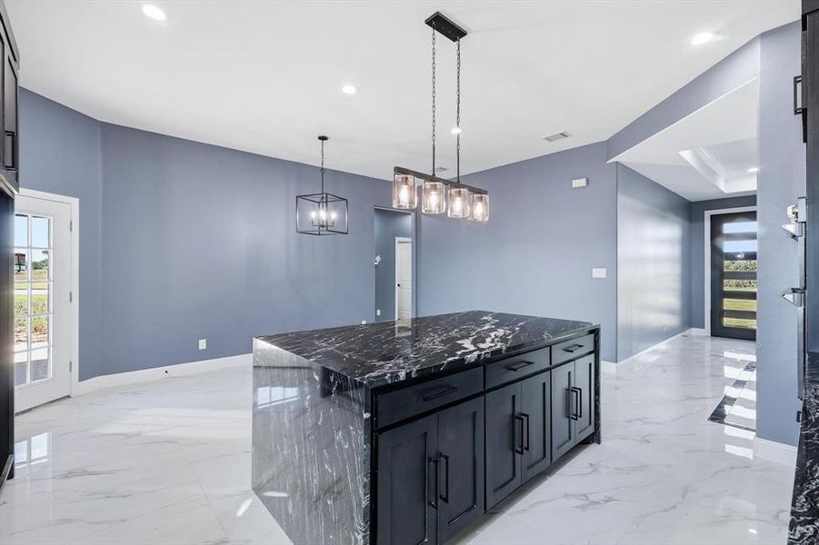 Kitchen featuring dark cabinets, dark stone counters, a kitchen island, hanging light fixtures, and recessed lighting
