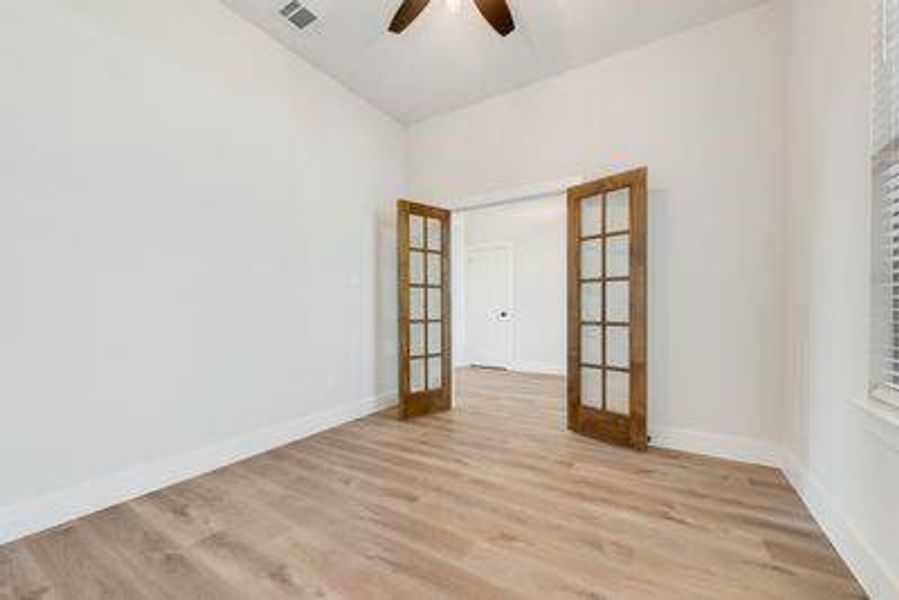 Empty room featuring french doors, vaulted ceiling, light wood-type flooring, and ceiling fan