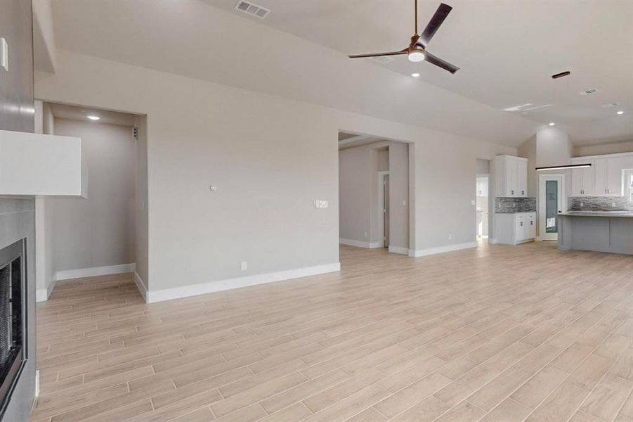 Unfurnished living room with light wood-type flooring, visible vents, a ceiling fan, a fireplace, and vaulted ceiling