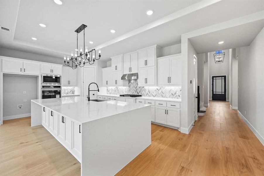 Kitchen featuring decorative backsplash, white cabinetry, a chandelier, a tray ceiling, and recessed lighting