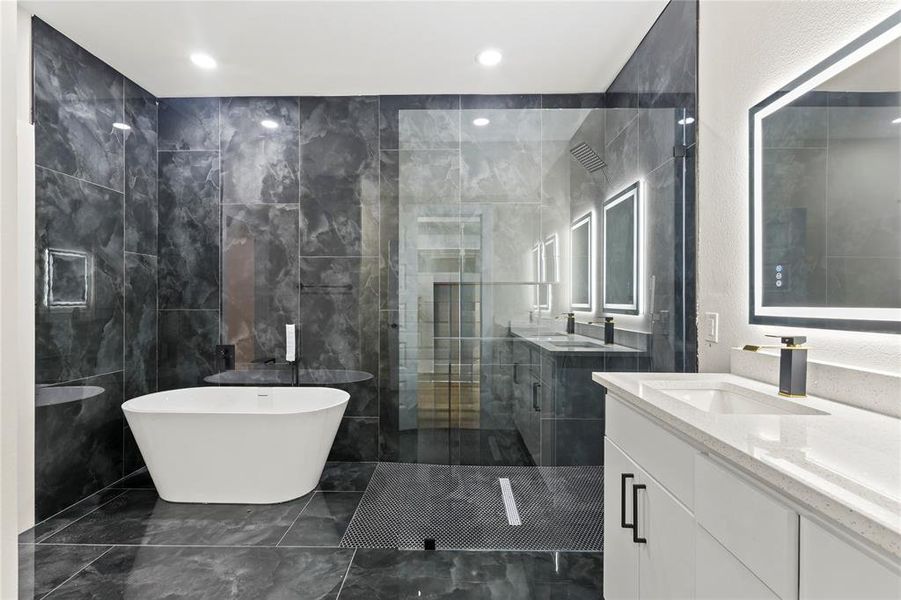 Full bathroom with two vanities, a freestanding bath, a stall shower, tile walls, and dark marble finish floors