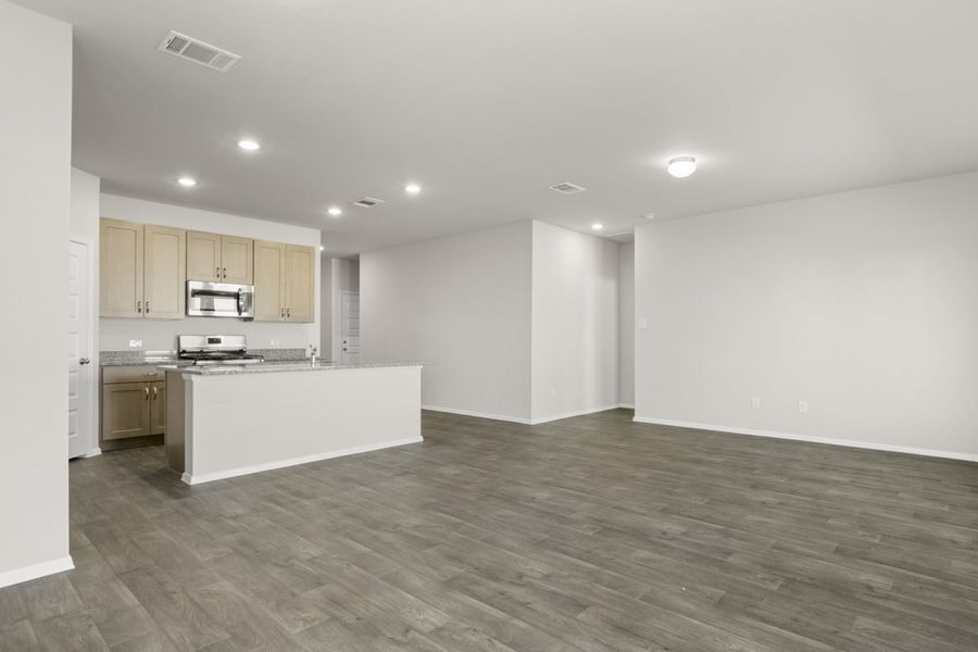 Image of a dining room area with dark vinyl flooring, cream walls, and a kitchen with a center island