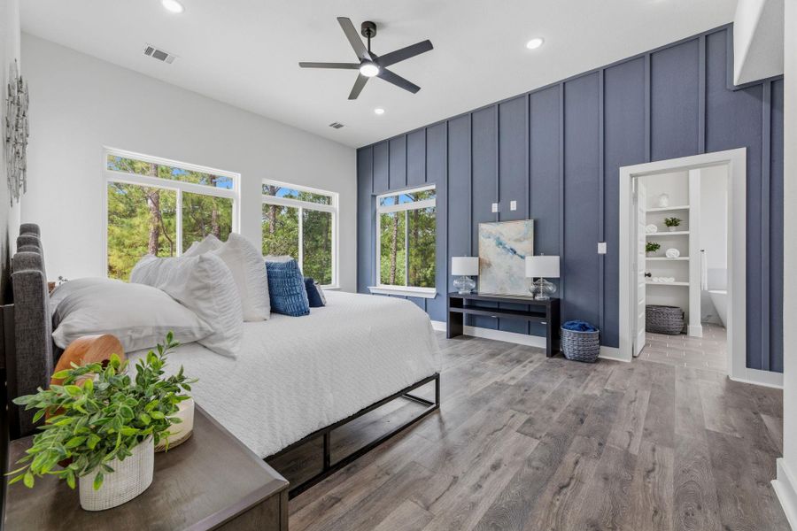 A primary bedroom offering ample natural light, a wood-paneled accent wall, and a view of the outdoors.