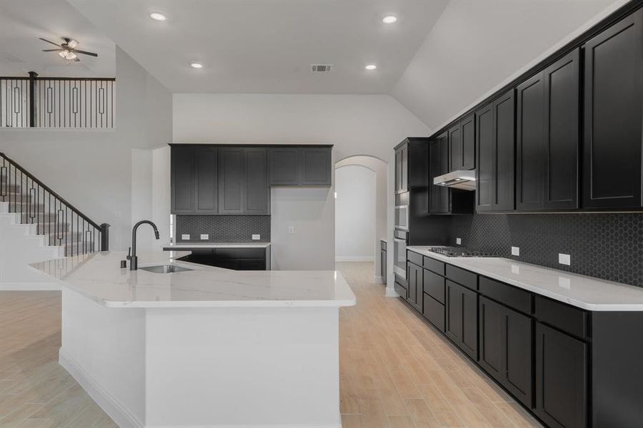 Kitchen featuring backsplash, light stone counters, sink, ceiling fan, and vaulted ceiling