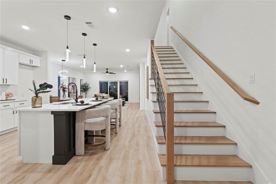 Kitchen featuring white cabinets, a breakfast bar, pendant lighting, light wood-style flooring, and a kitchen island with sink Kitchen featuring white cabinets, a breakfast bar, pendant lighting, light wood-style flooring, and a kitchen island with sink