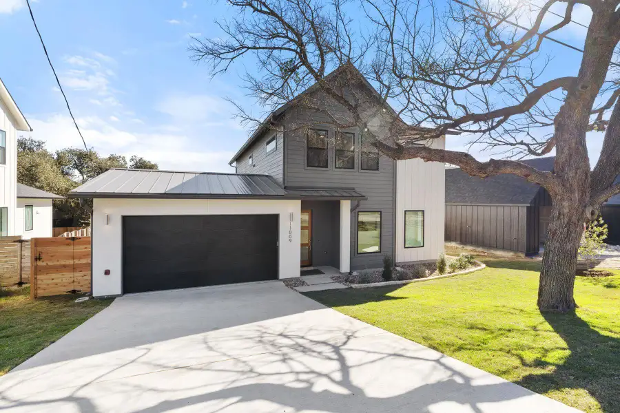 View of front facade with a garage, driveway, metal roof, and fence