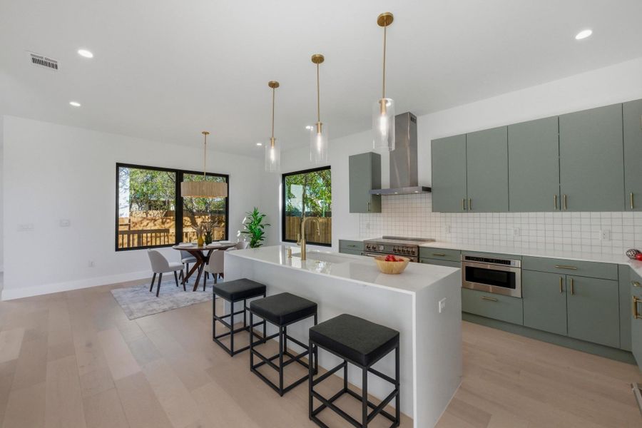 Kitchen featuring a center island with sink, decorative backsplash, hanging light fixtures, wall chimney range hood, and recessed lighting