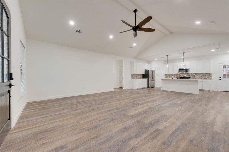 Unfurnished living room with light hardwood / wood-style floors, high vaulted ceiling, beam ceiling, and ceiling fan