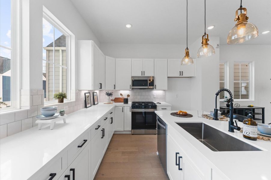 Bright and beautifully functional, this kitchen is anchored by an expansive countertop that offers ample prep space and casual seating—perfect for everything from morning coffee to evening entertaining. Two large windows bathe the space in natural light, framing outdoor views and enhancing the airy, open feel. Clean lines, modern finishes, and thoughtful design make this kitchen a true centerpiece of the home.