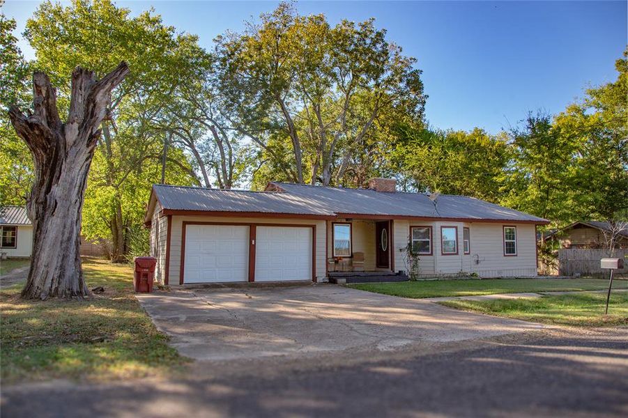 View of front of house with driveway, a metal roof, a garage, a front lawn, and a chimney