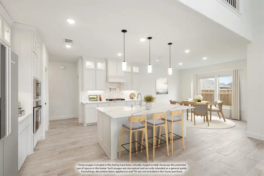 Open kitchen with white cabinets, large island with bar seating, pendant lights, and adjacent dining area with light wood floors.