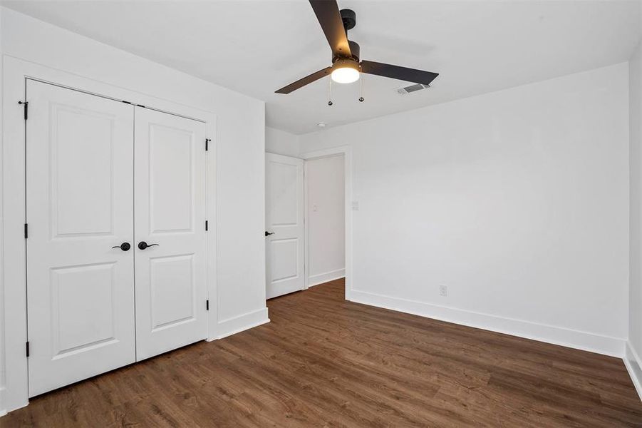 Unfurnished bedroom featuring a ceiling fan, baseboards, visible vents, dark wood-type flooring, and a closet