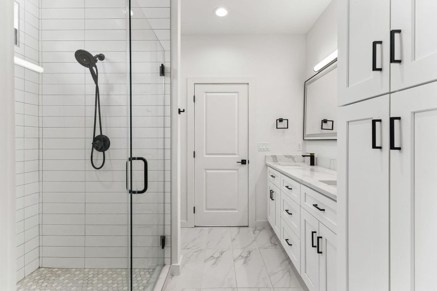 Shower enclosure with matte black fixtures, white subway tile surround, and pebble-style floor