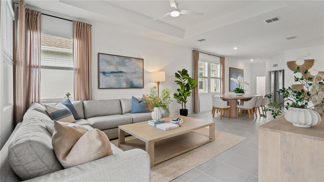 Living room with light tile patterned flooring, a ceiling fan, and a raised ceiling Living room with light tile patterned flooring, a ceiling fan, and a raised ceiling