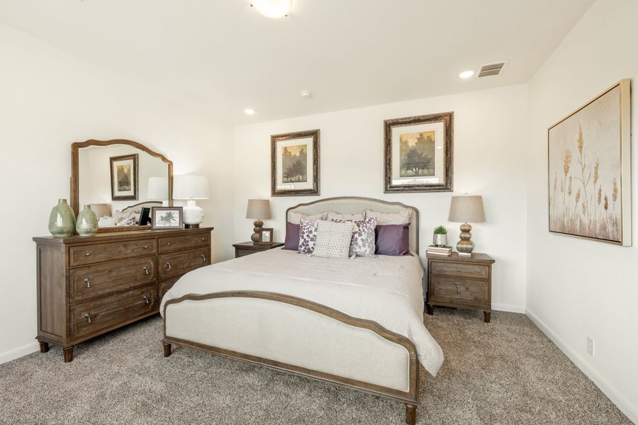 Bedroom with upholstered bed, wood dresser with mirror, and carpet flooring
