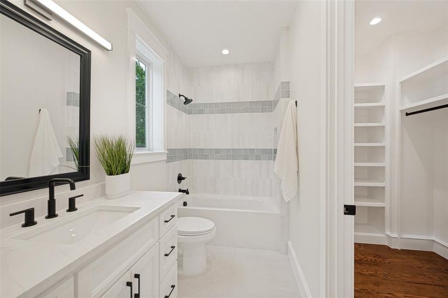 Bathroom featuring a white vanity with an integrated sink, matte black fixtures, a framed mirror, and a tub/shower combination with decorative tile banding