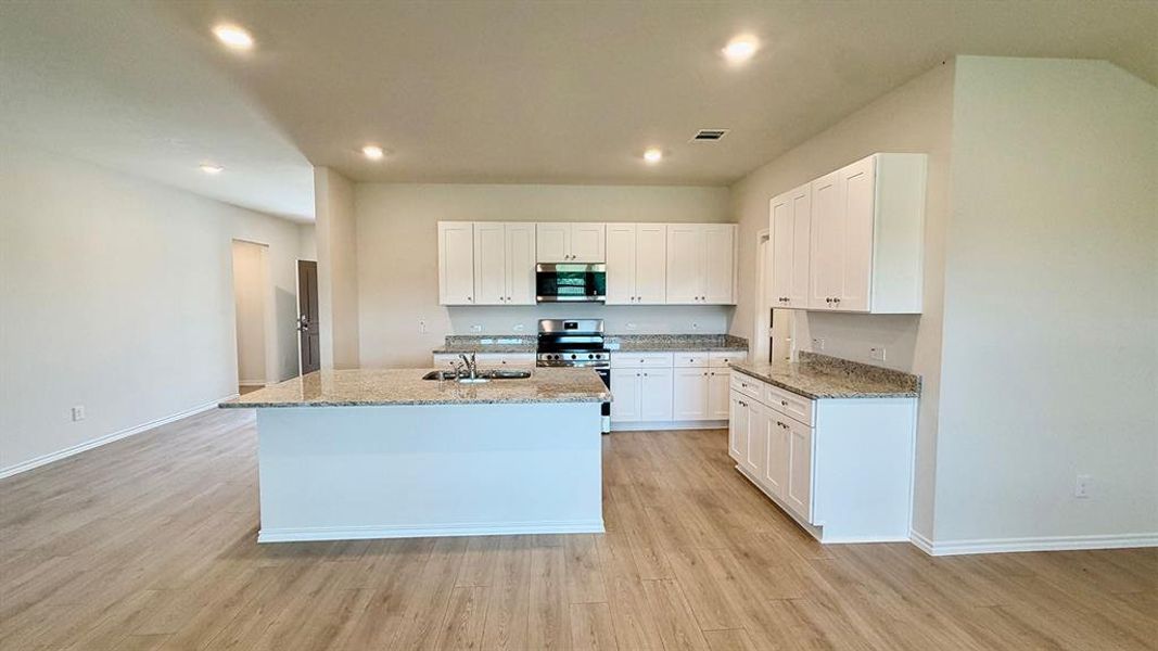 Open-concept kitchen with a central island, recessed lighting, wood-finish flooring, white cabinetry, and light-toned countertops