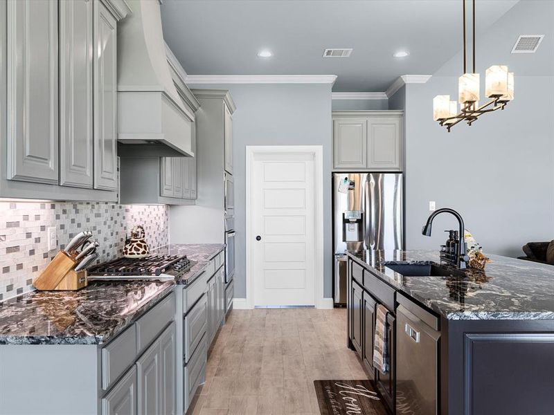 Kitchen with dark stone counters, ornamental molding, hanging light fixtures, tasteful backsplash, and appliances with stainless steel finishes Kitchen with dark stone counters, ornamental molding, hanging light fixtures, tasteful backsplash, and appliances with stainless steel finishes