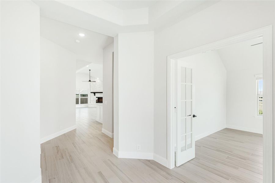 Bright hallway with light wood floors, French door, and open view to living area with ceiling fan