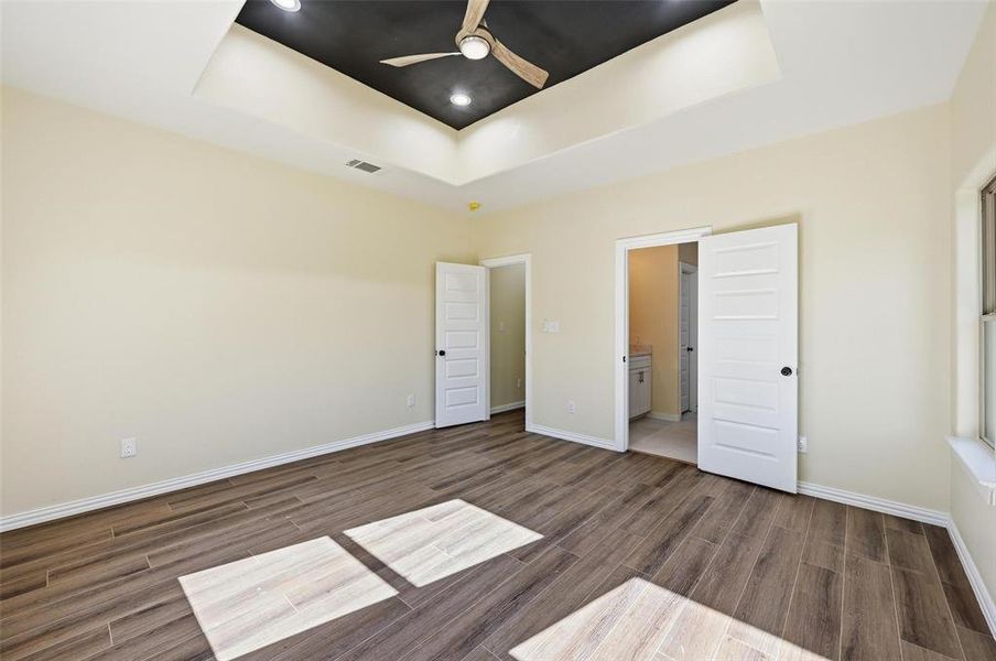 Unfurnished bedroom with a raised ceiling, wood tiled floors, ceiling fan, and ensuite bath Unfurnished bedroom with a raised ceiling, wood tiled floors, ceiling fan, and ensuite bath