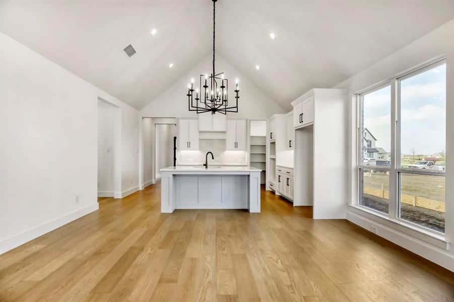 Kitchen featuring a high ceiling, an island with sink, white cabinets, hanging lights, and light wood-style flooring