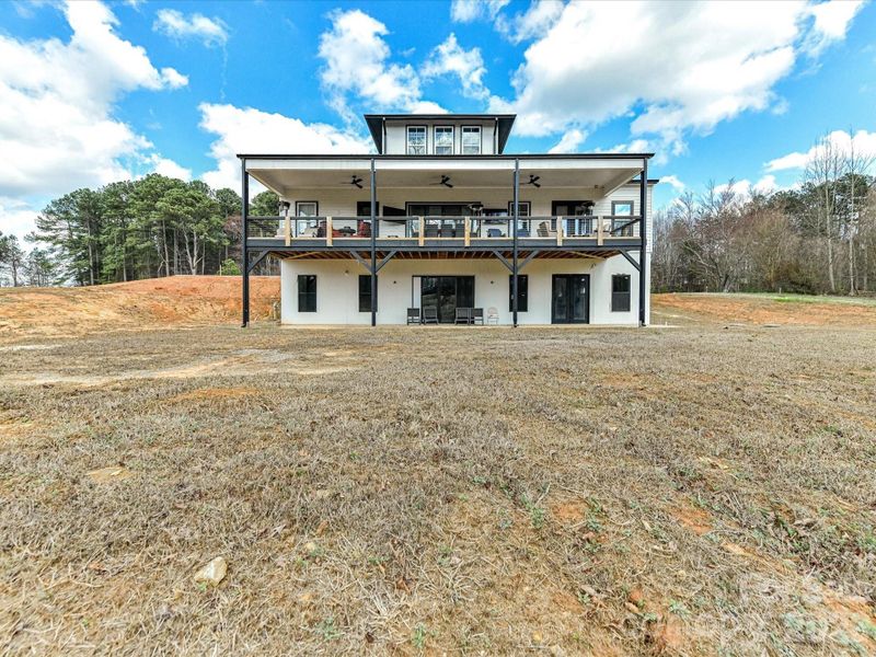 Back of the home featuring a large covered deck, lower-level patio, and expansive yard with plenty of space for outdoor living.
