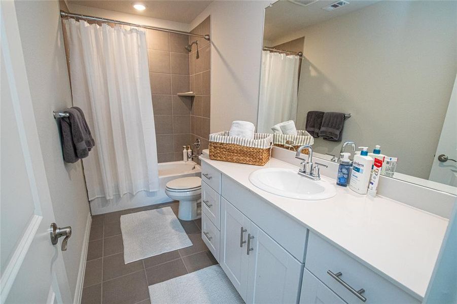 Full bath with shower / bath combo, vanity, and dark tile patterned floors Full bath with shower / bath combo, vanity, and dark tile patterned floors