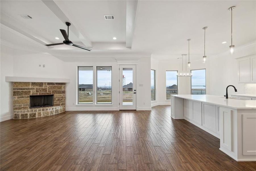 Unfurnished living room with dark hardwood / wood-style flooring, sink, a stone fireplace, ceiling fan, and beam ceiling