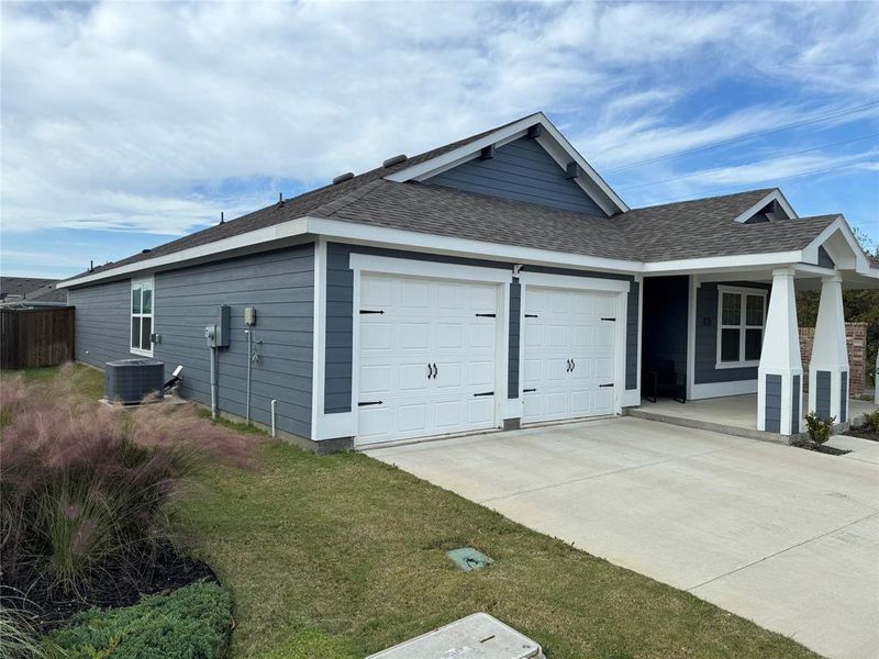 View of property exterior with a garage, cooling unit, and a lawn