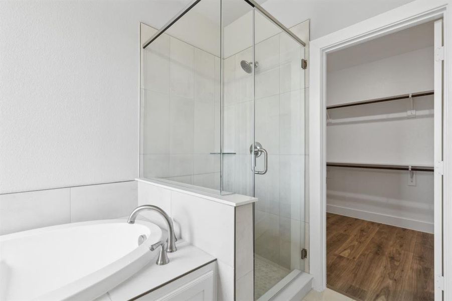 Full bath featuring a spacious closet, a shower stall, a bath, and wood finished floors Full bath featuring a spacious closet, a shower stall, a bath, and wood finished floors