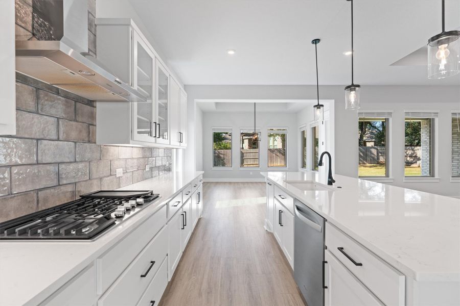 Kitchen featuring white cabinets, wall chimney exhaust hood, hanging light fixtures, light wood-style flooring, and glass insert cabinets