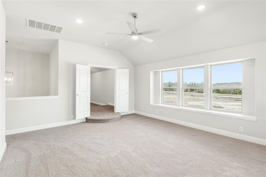 Spacious bedroom with vaulted ceiling, ceiling fan, carpet flooring, and large windows with outdoor views Spacious bedroom with vaulted ceiling, ceiling fan, carpet flooring, and large windows with outdoor views
