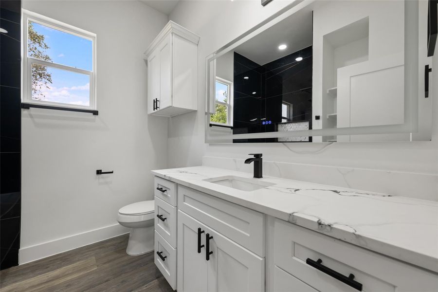 Modern bathroom featuring a white vanity with integrated sink, a large backlit mirror, and dark wood-finish flooring