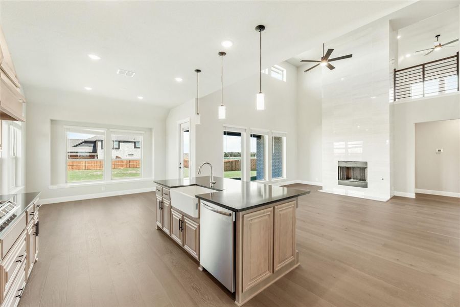 Open-concept kitchen with large island, dark countertops, and high ceilings opening to living room with fireplace Open-concept kitchen with large island, dark countertops, and high ceilings opening to living room with fireplace