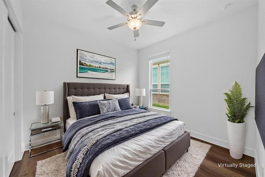 Bright bedroom featuring a large window, dark wood-finish flooring, a ceiling fan with integrated lighting, and a white interior door