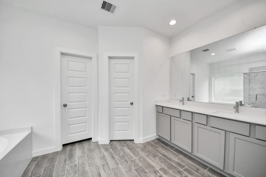 Escape to a spa-like oasis in this primary bathroom. Enjoy a walk-in shower with tile surround, a separate garden tub with custom detailing, and an elegant vanity featuring light countertops, modern hardware, and beautiful vanity lights. Experience luxury and relaxation in every detail. Escape to a spa-like oasis in this primary bathroom. Enjoy a walk-in shower with tile surround, a separate garden tub with custom detailing, and an elegant vanity featuring light countertops, modern hardware, and beautiful vanity lights. Experience luxury and relaxation in every detail.