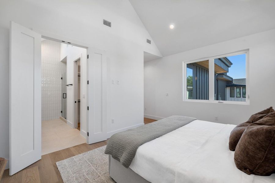 Bedroom with high vaulted ceiling, light wood-style flooring, ensuite bathroom, and recessed lighting Bedroom with high vaulted ceiling, light wood-style flooring, ensuite bathroom, and recessed lighting