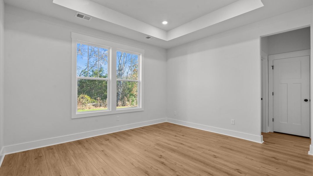 Elegant primary suite with hardwood flooring, tray ceiling, and superior natural light in this accomplished DRB Homes design Elegant primary suite with hardwood flooring, tray ceiling, and superior natural light in this accomplished DRB Homes design