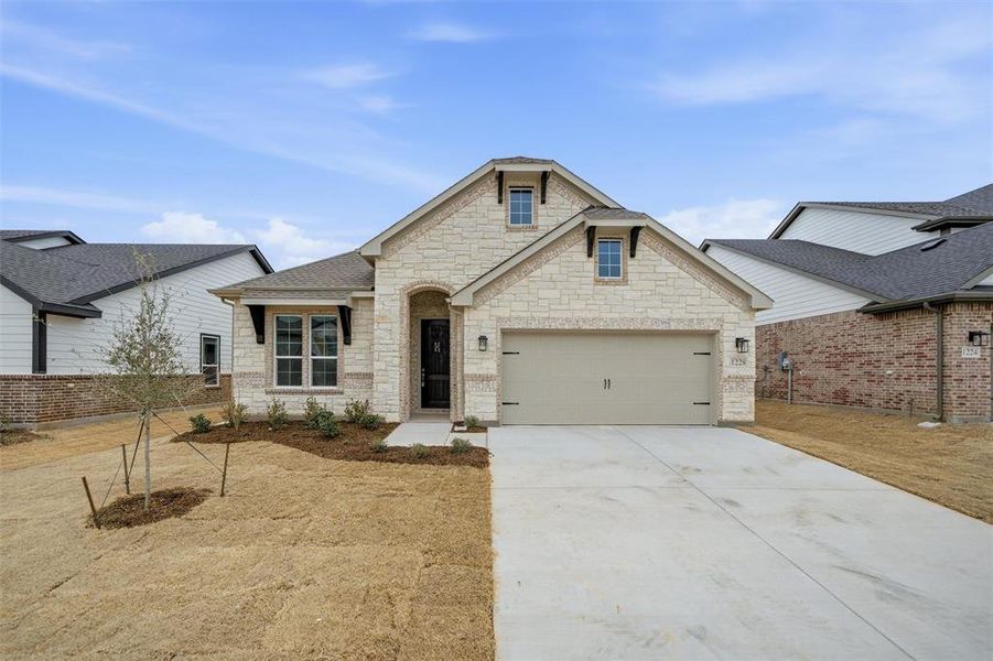 View of front of property featuring driveway, an attached garage, stone siding, and a shingled roof