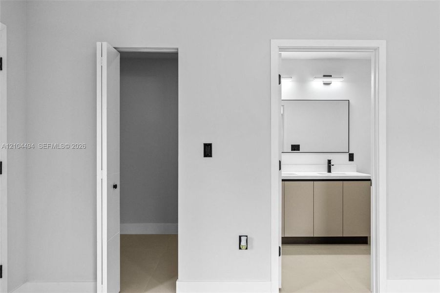 Bathroom featuring a double-sink vanity with light-toned cabinetry, a rectangular mirror with a dark frame, wall-mounted light fixtures, and a matte black faucet