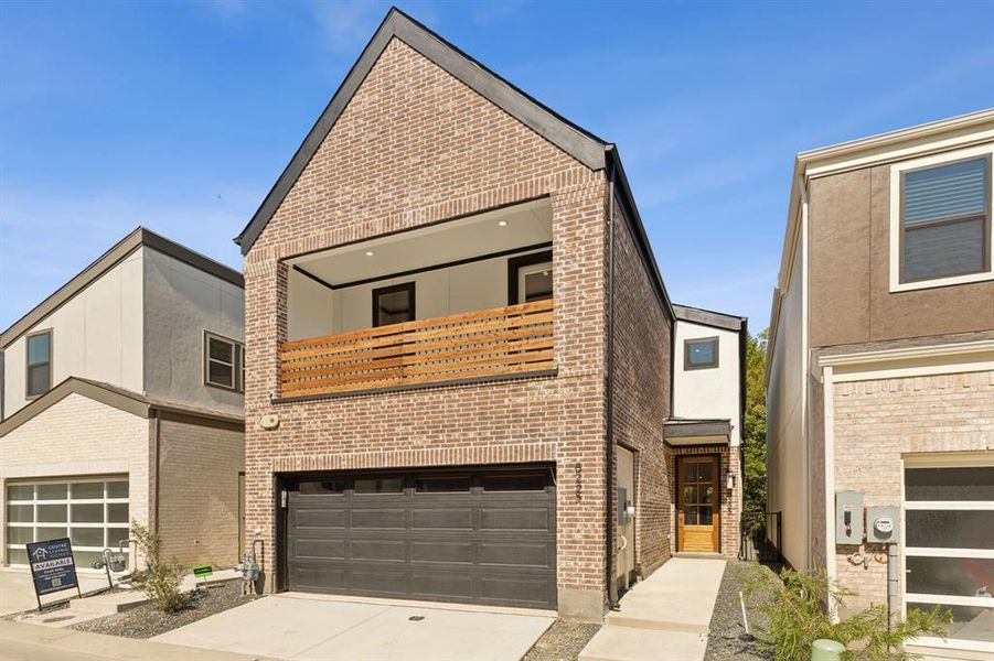 View of front of house with concrete driveway, brick siding, an attached garage, and a balcony