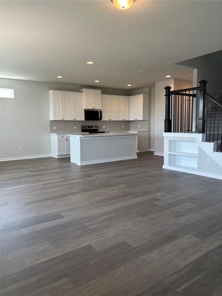 Kitchen featuring white cabinets, open floor plan, a center island with sink, appliances with stainless steel finishes, and dark wood-type flooring