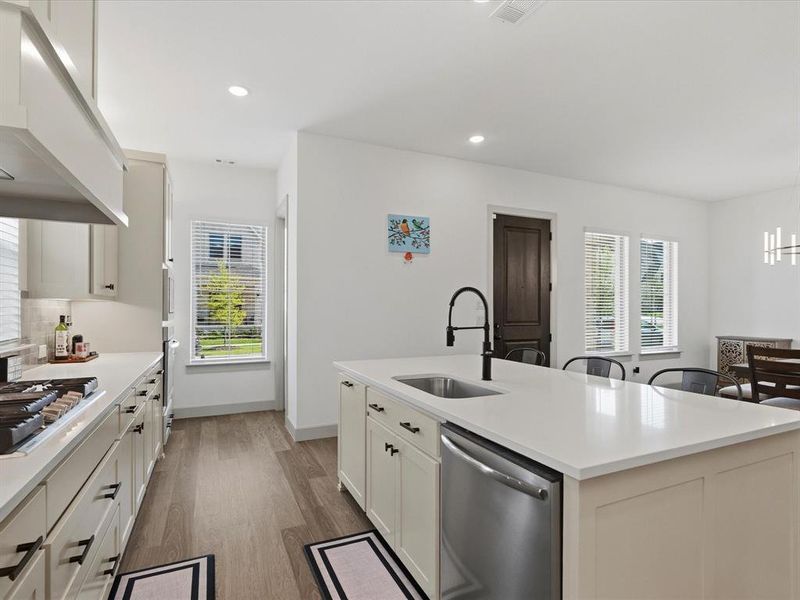 Modern kitchen featuring light-toned cabinetry, stainless steel appliances, and a central island with a sink and seating area
