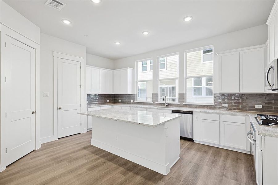 This kitchen features modern white cabinetry, a large central island with a light-colored countertop, and a sleek grey subway tile backsplash